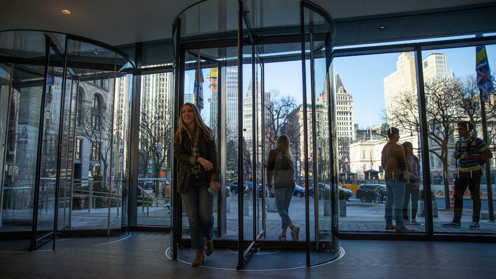  students walking through revolving doors of One  Plaza at the New York City Campus