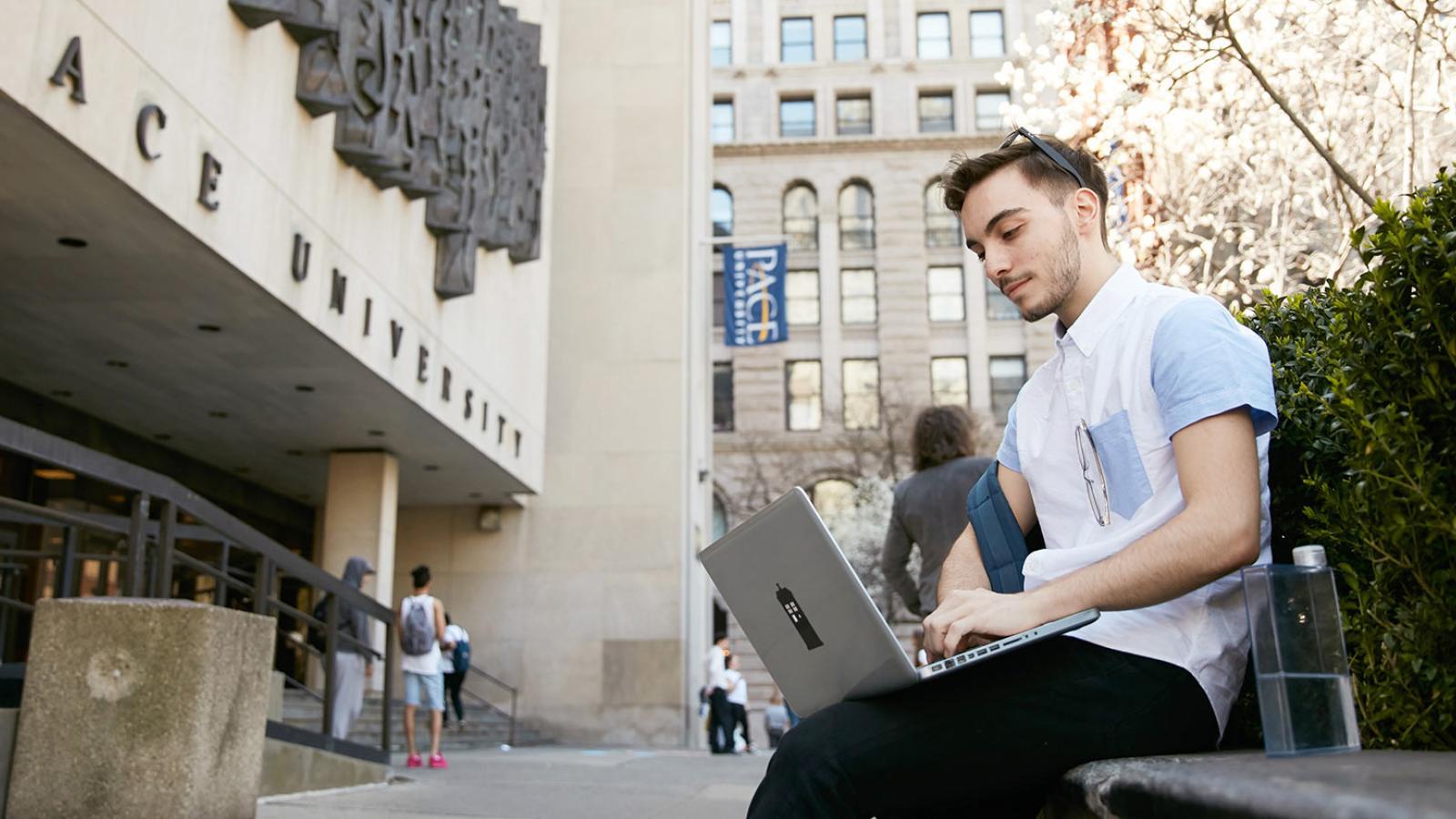 Student sitting in front of 1  Plaza looking at his laptop.