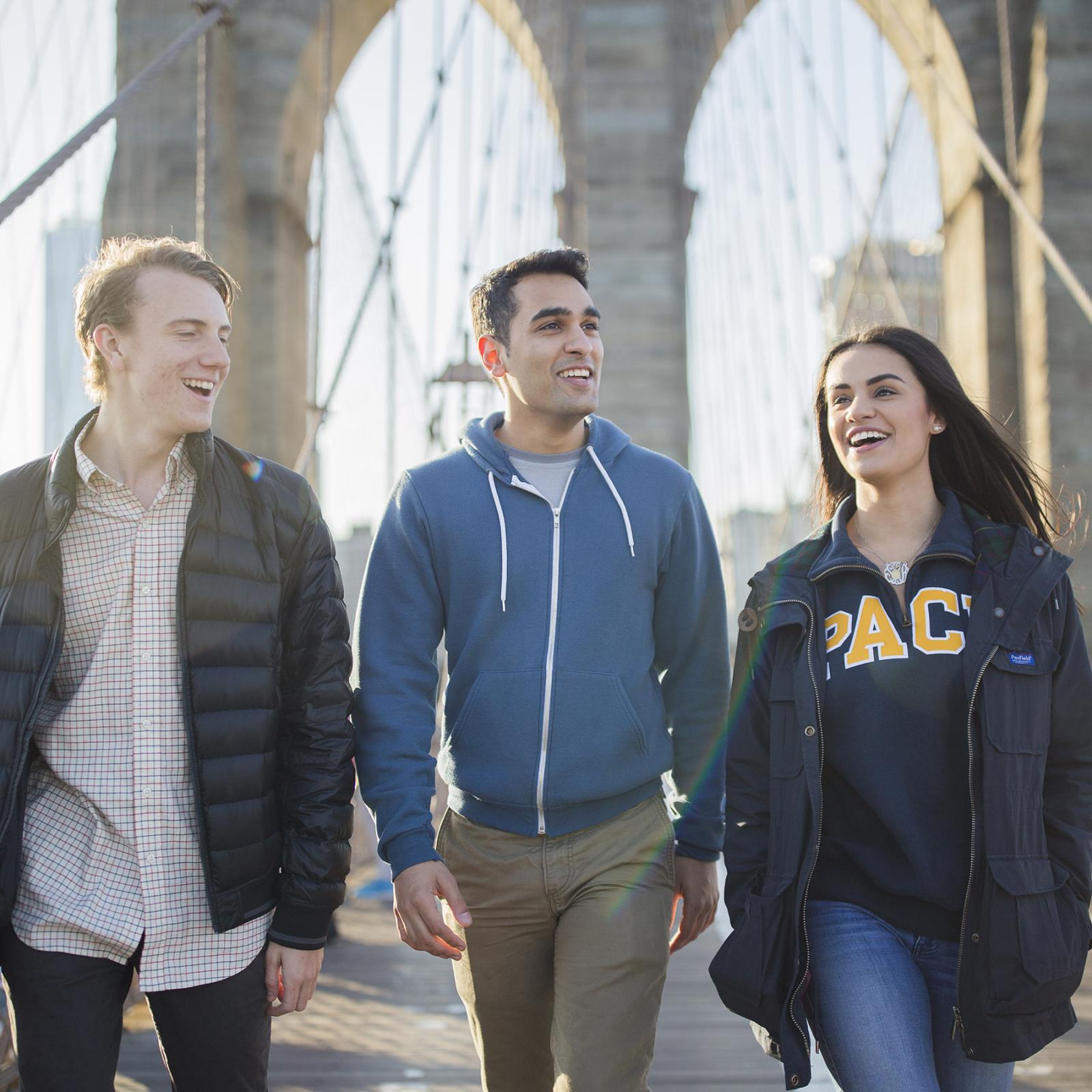 Three  Univesity students walking across the Brooklyn Bridge.