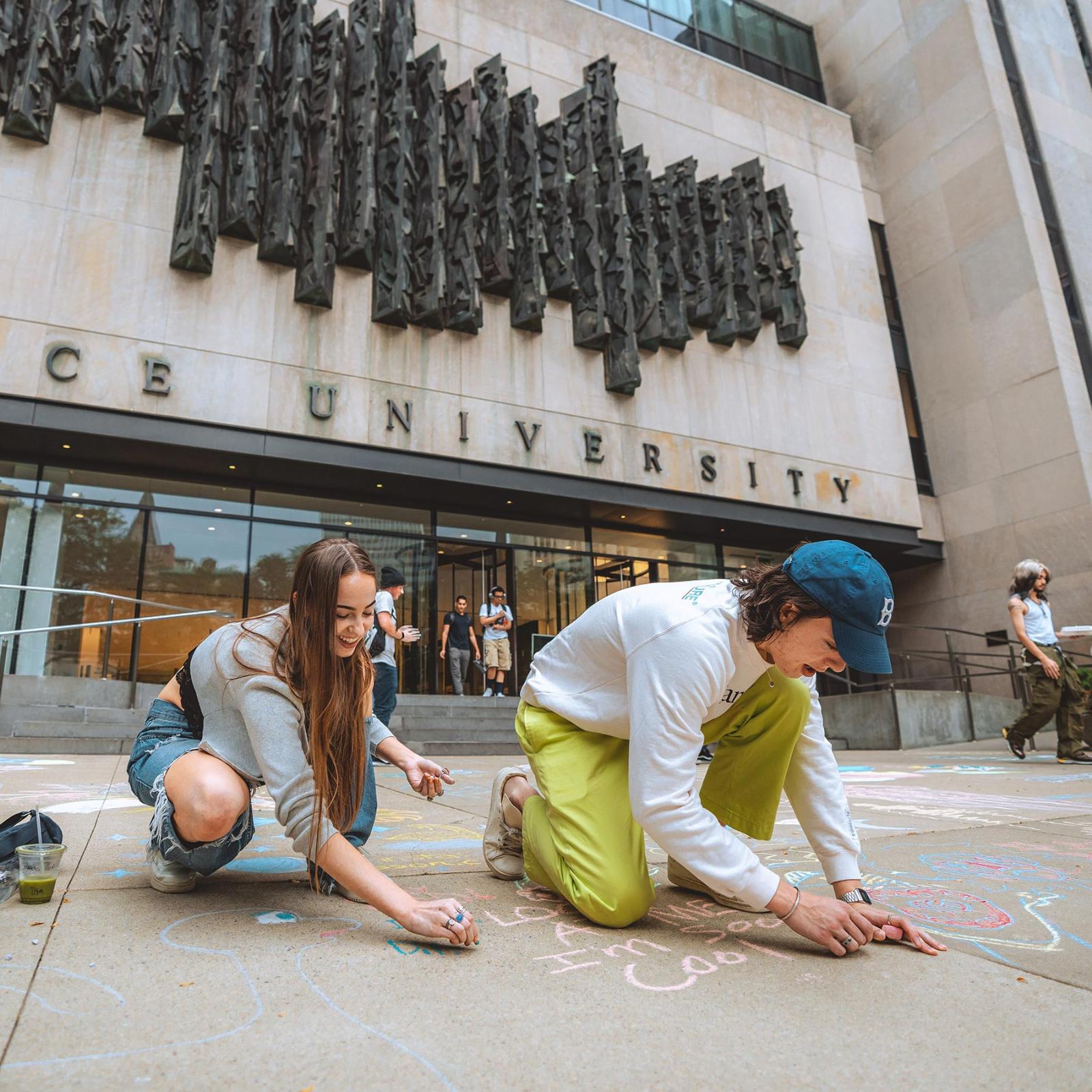 two students chalking in the front of One  Plaza