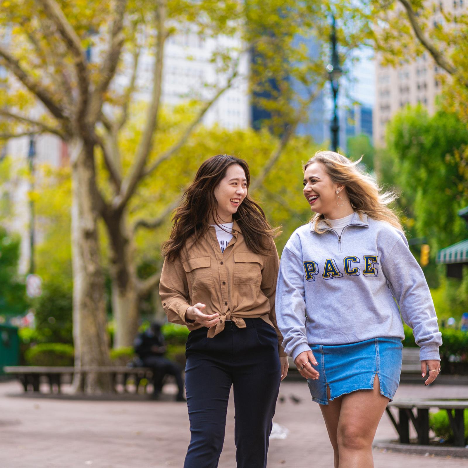 two  students walk through a park near the NYC campus