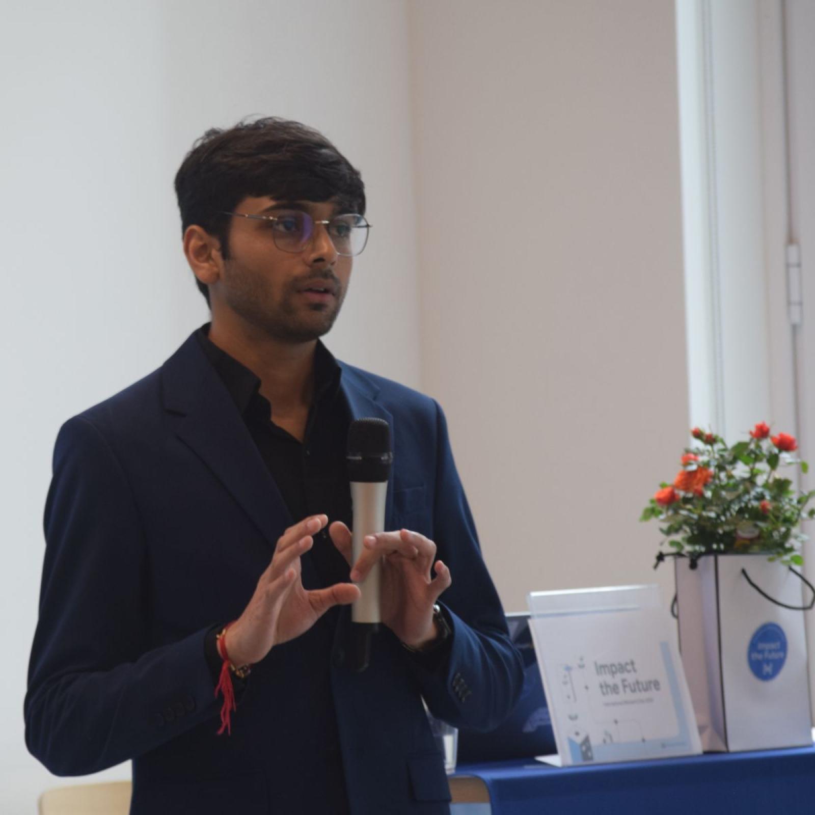  student Om Gaikhe holding a microphone while giving a speech during an event presentation.